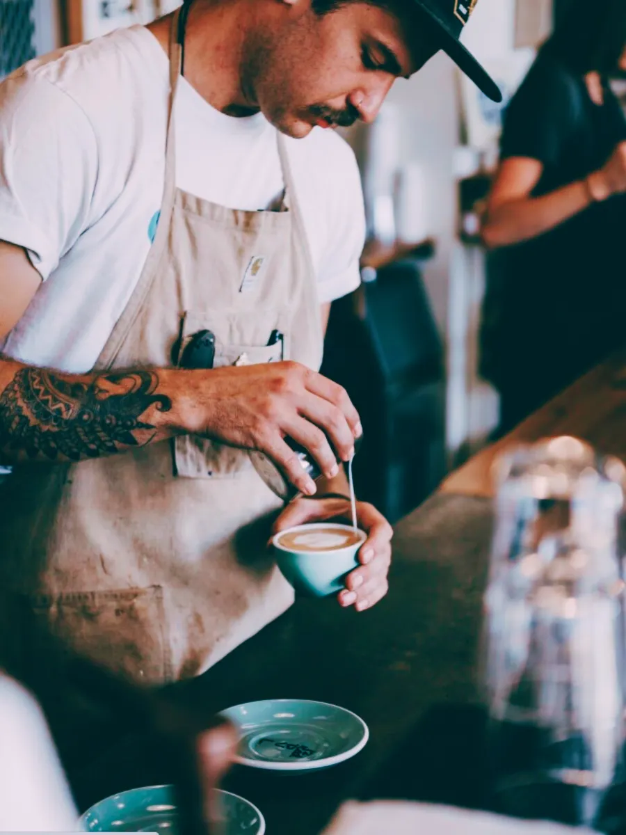 En man med tatueringar som är barista och häller upp kaffe.